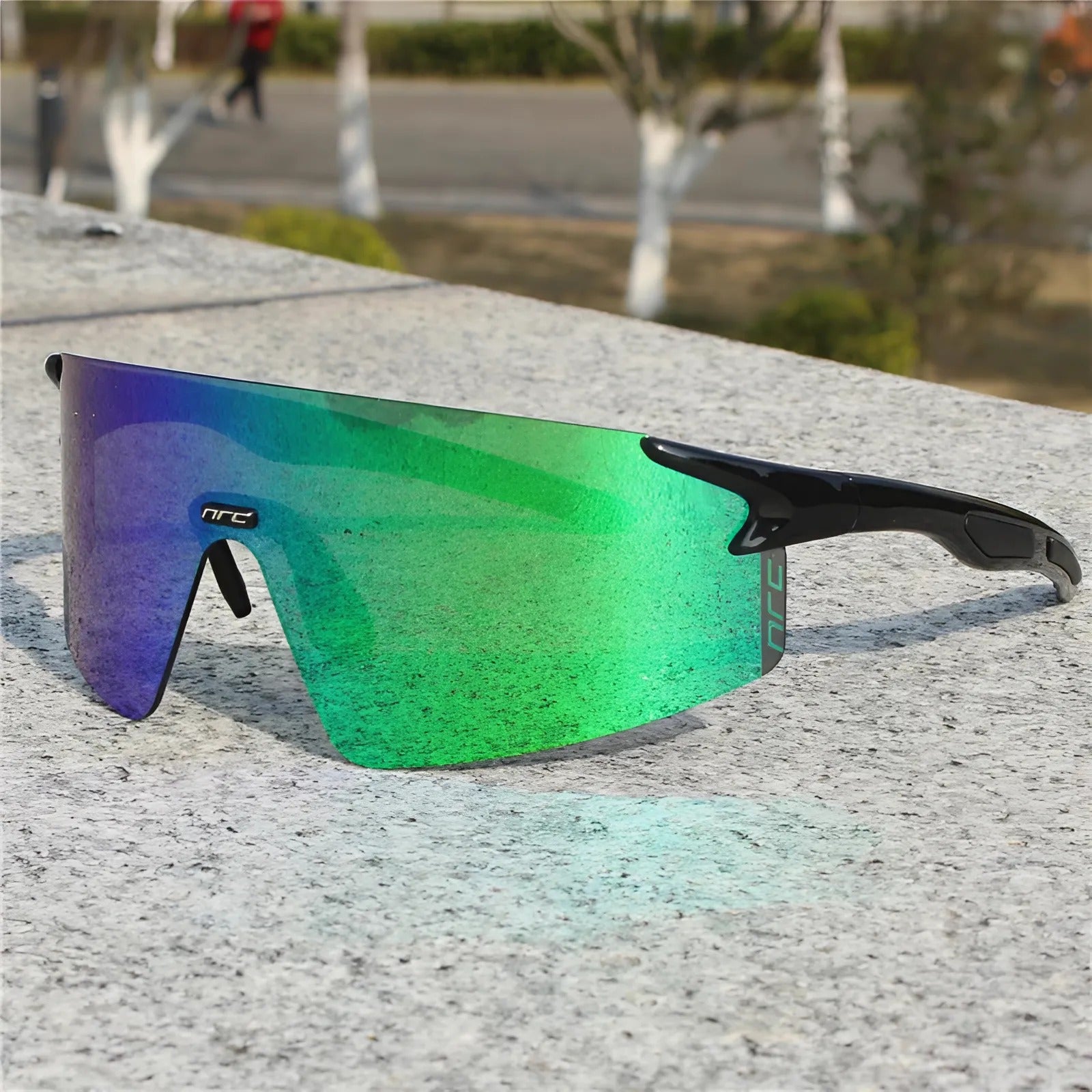Cycling sunglasses with green reflective lens and black frame resting on a stone surface