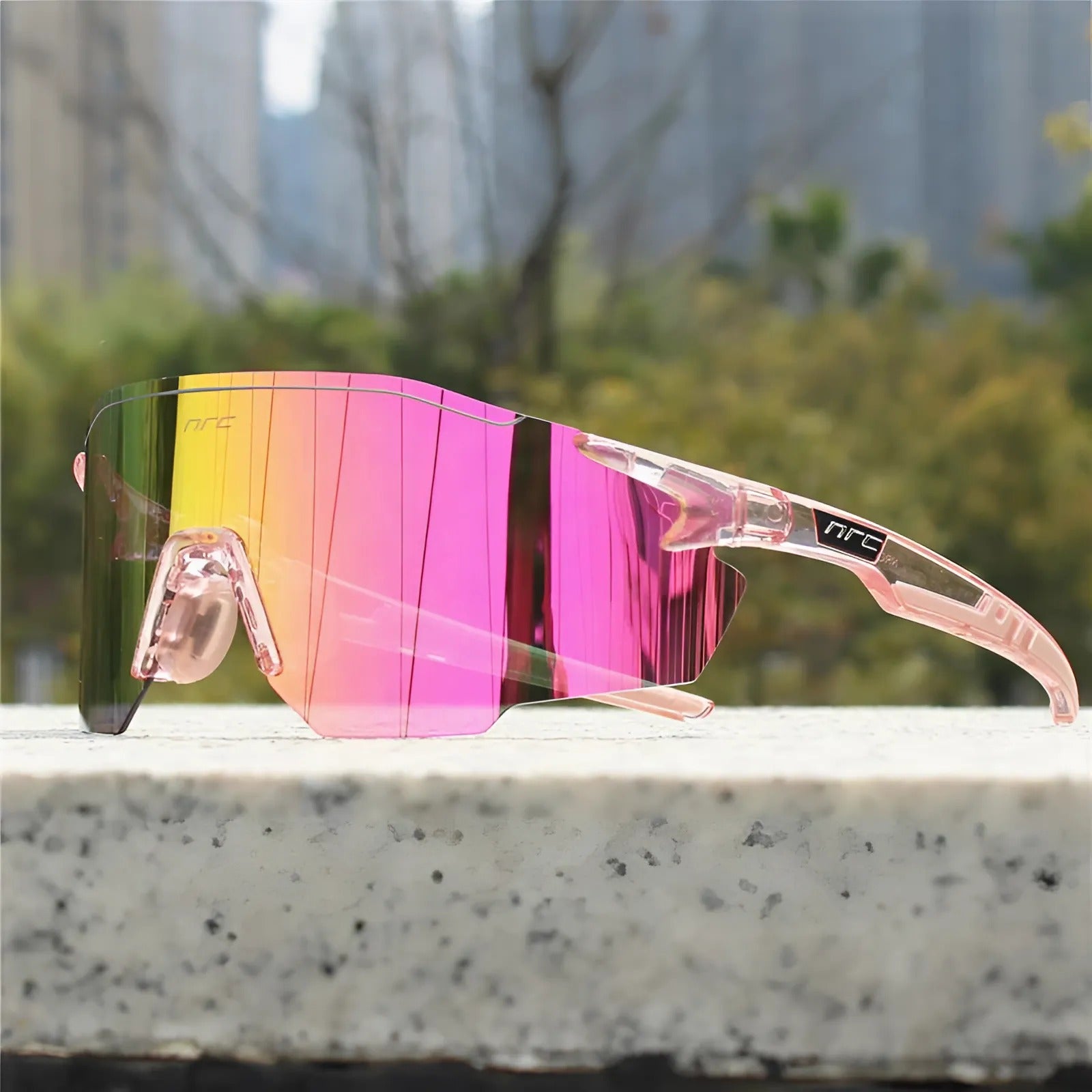 Cycling sunglasses with pink reflective lens and transparent clear frame resting on a stone surface