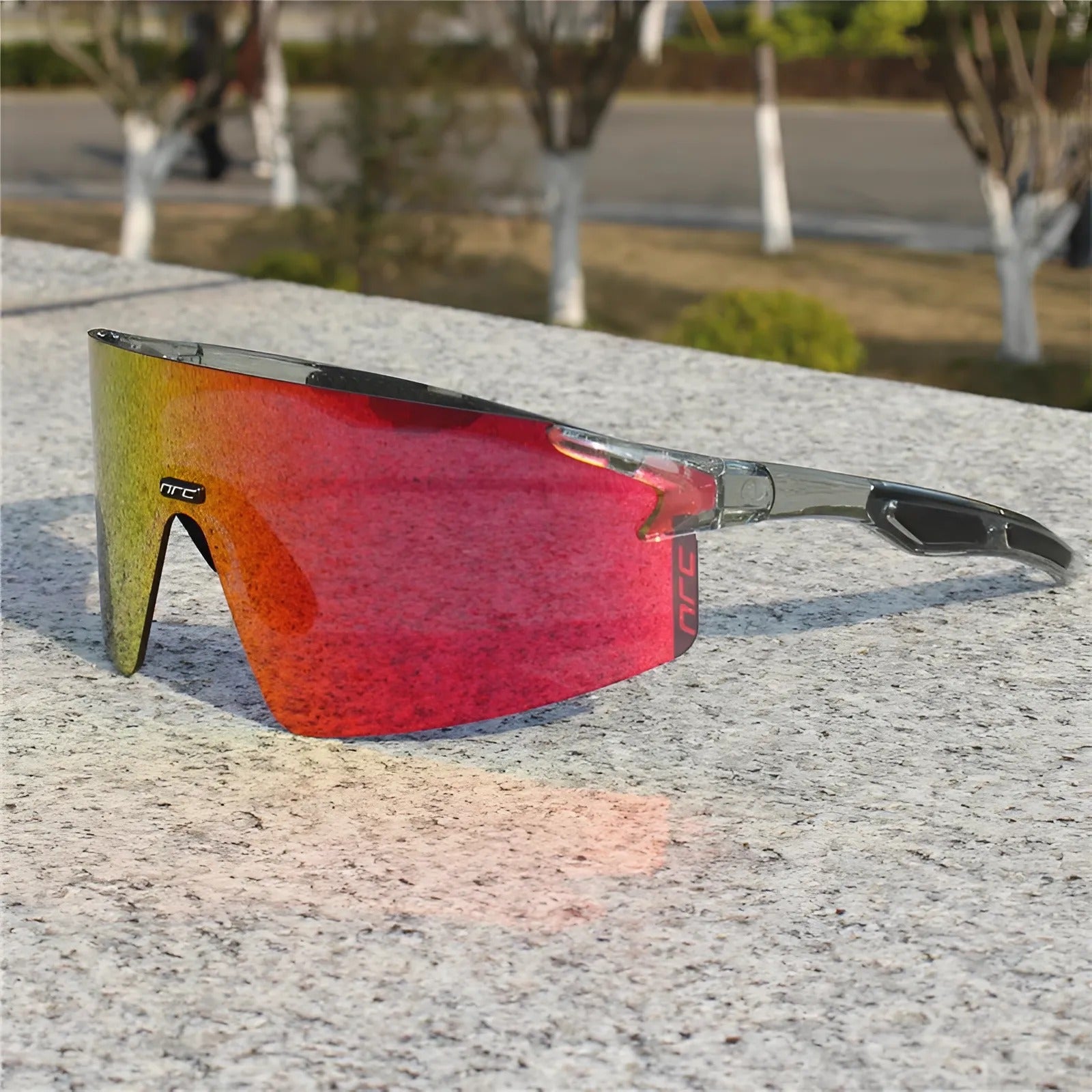 Cycling sunglasses with red reflective lens and grey frame resting on a stone surface