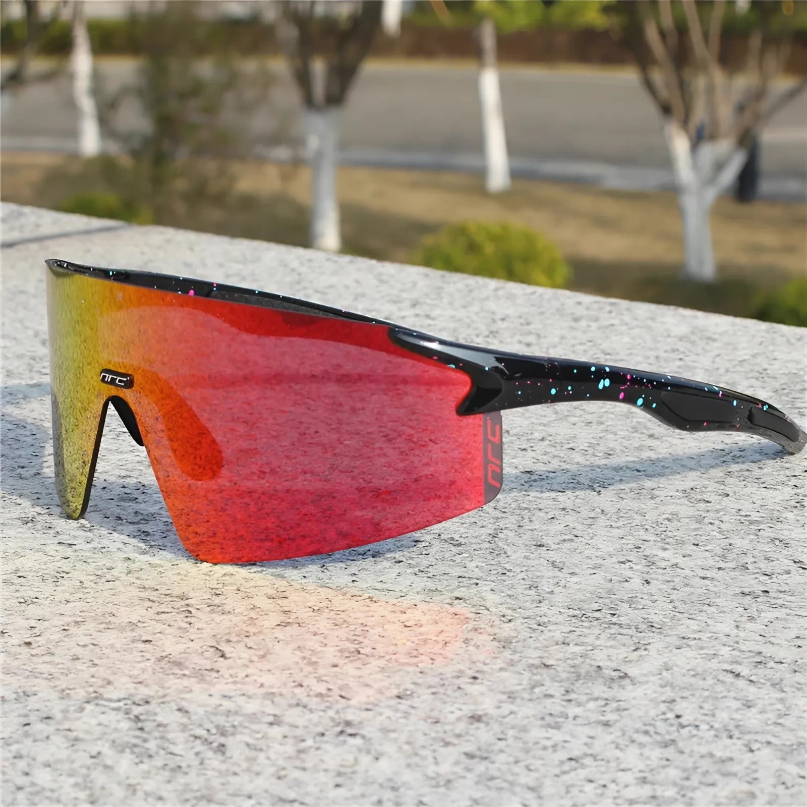 Cycling sunglasses with red reflective lens and black speckled frame resting on a stone surface