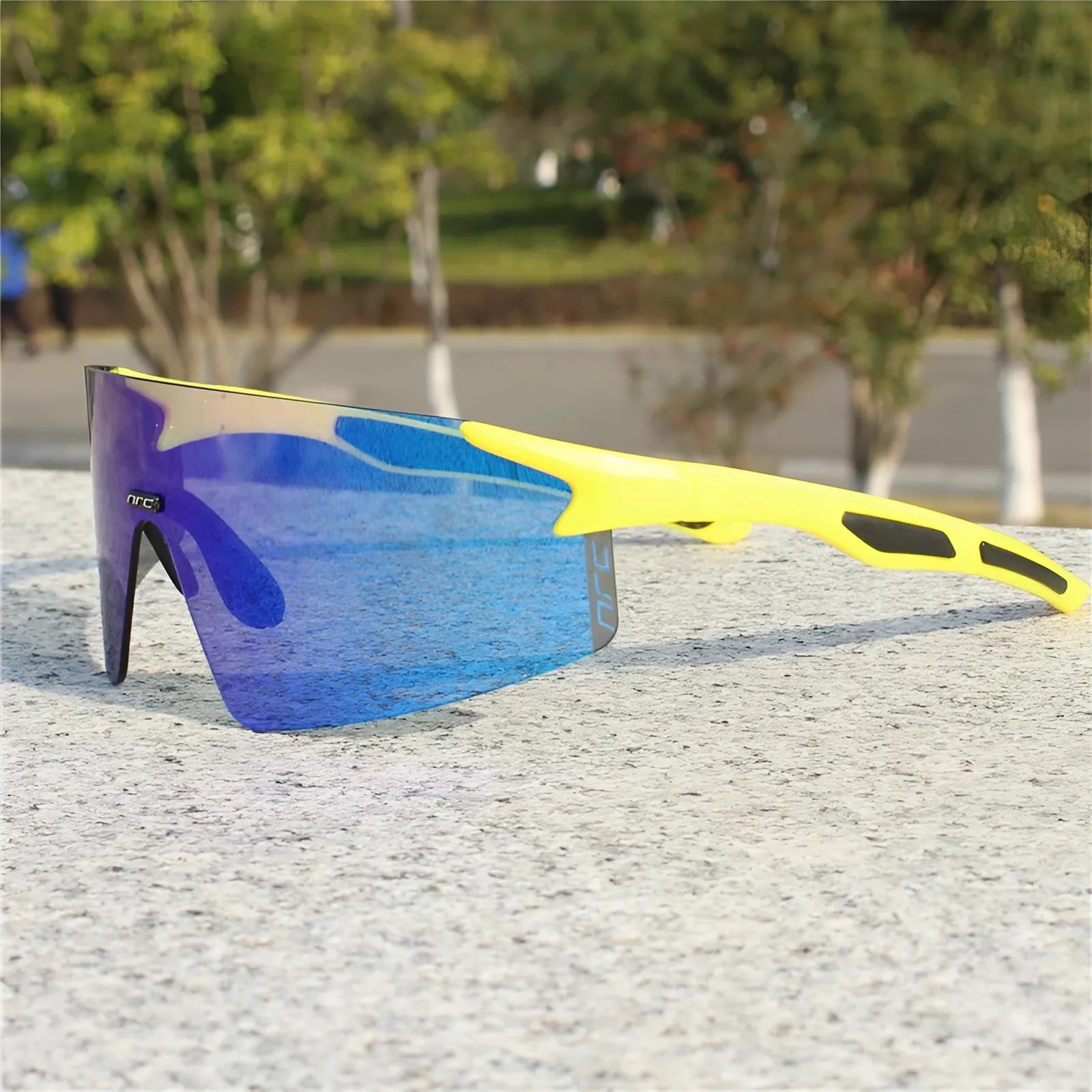 Cycling sunglasses with blue reflective lens and yellow frame resting on a stone surface