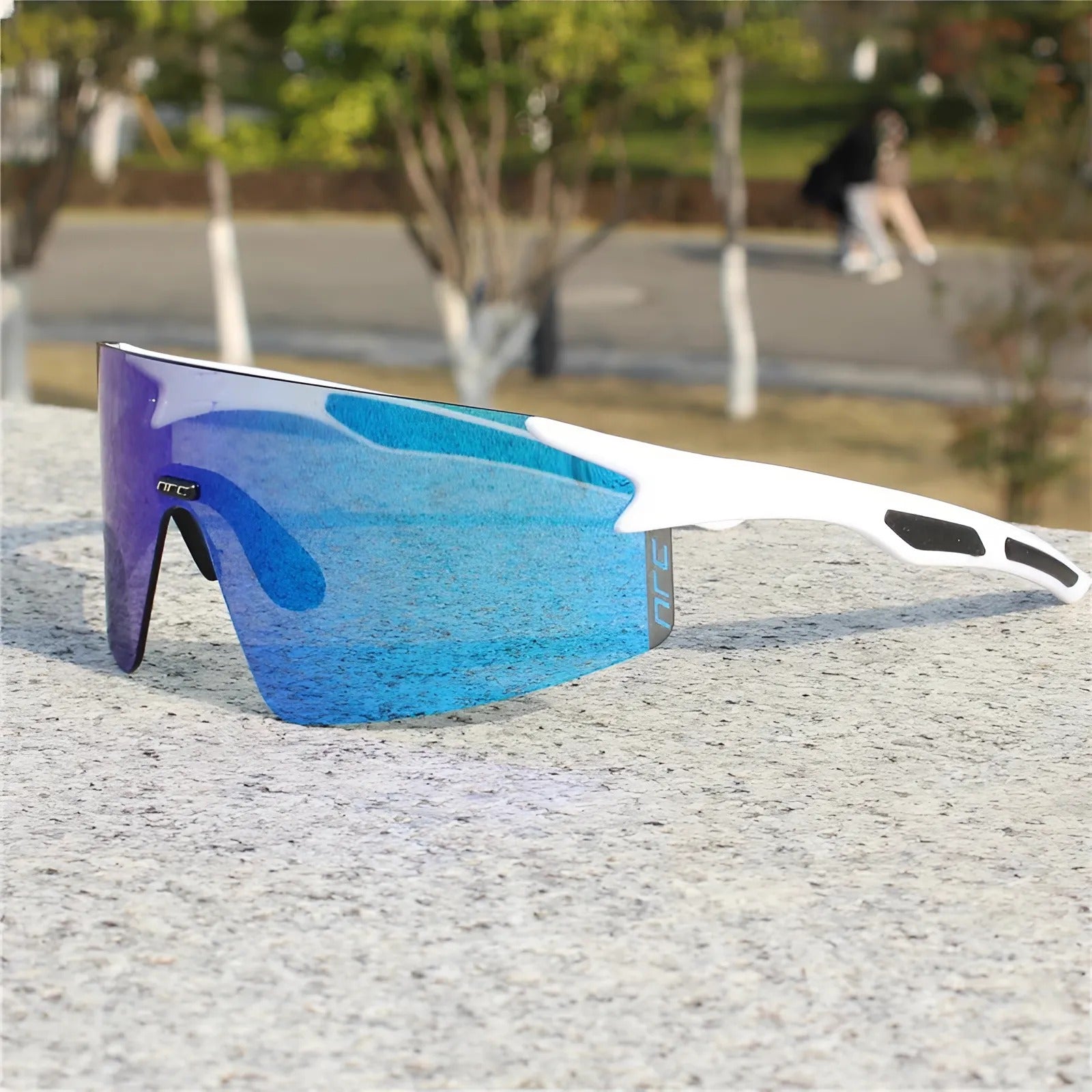Cycling sunglasses with blue reflective lens and white frame resting on a stone surface