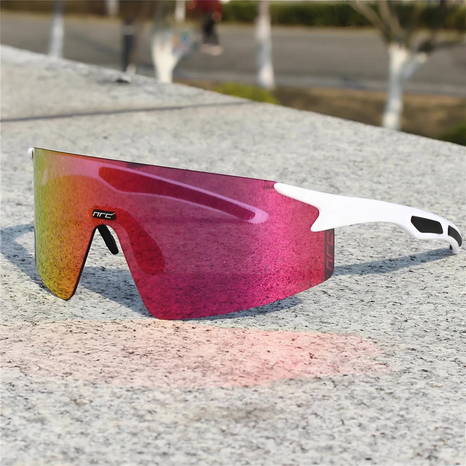 Cycling sunglasses with red reflective lens and white frame resting on a stone surface.